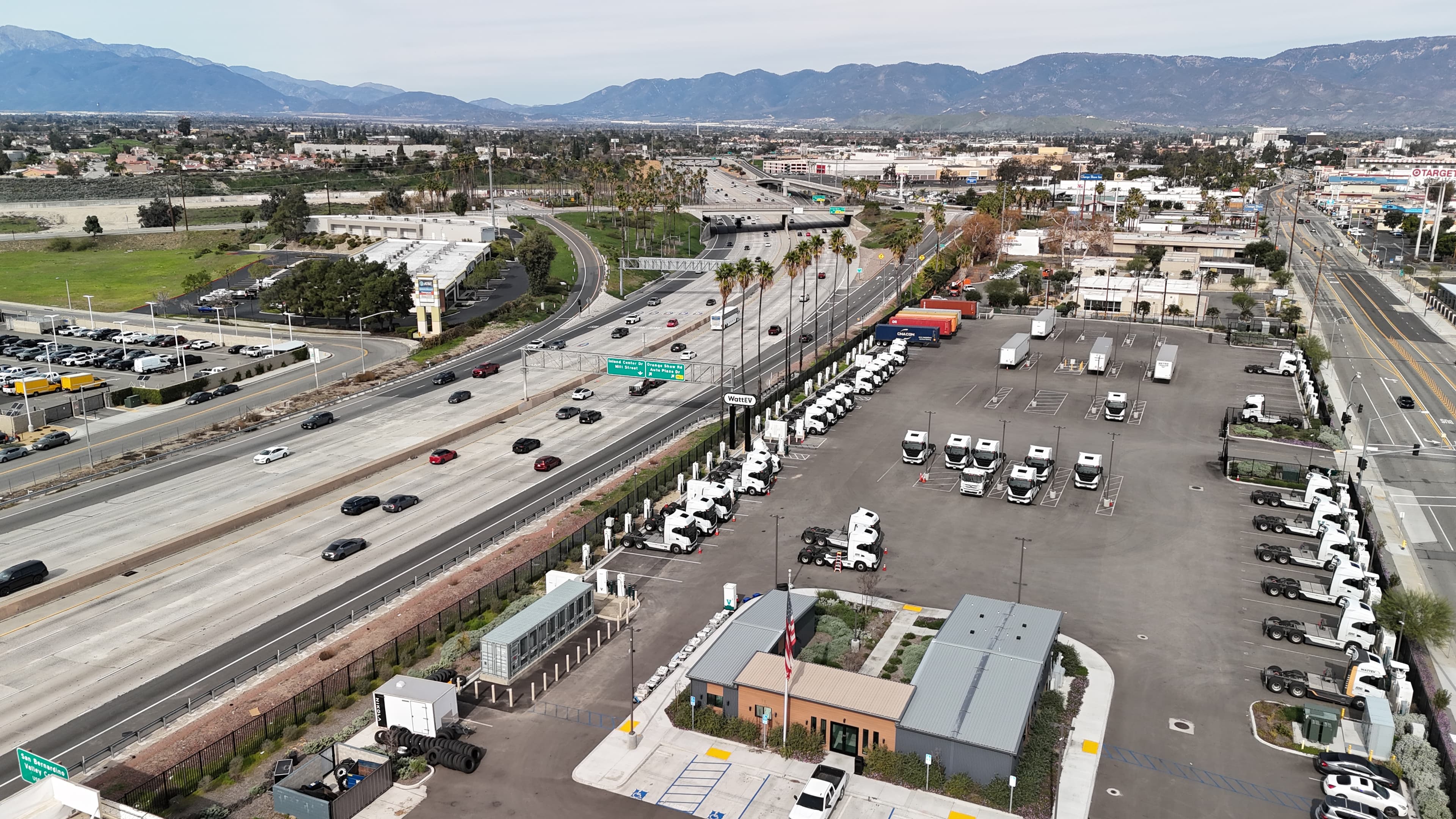 Aerial view of electric trucks charging at a WattEV depot beside a freeway